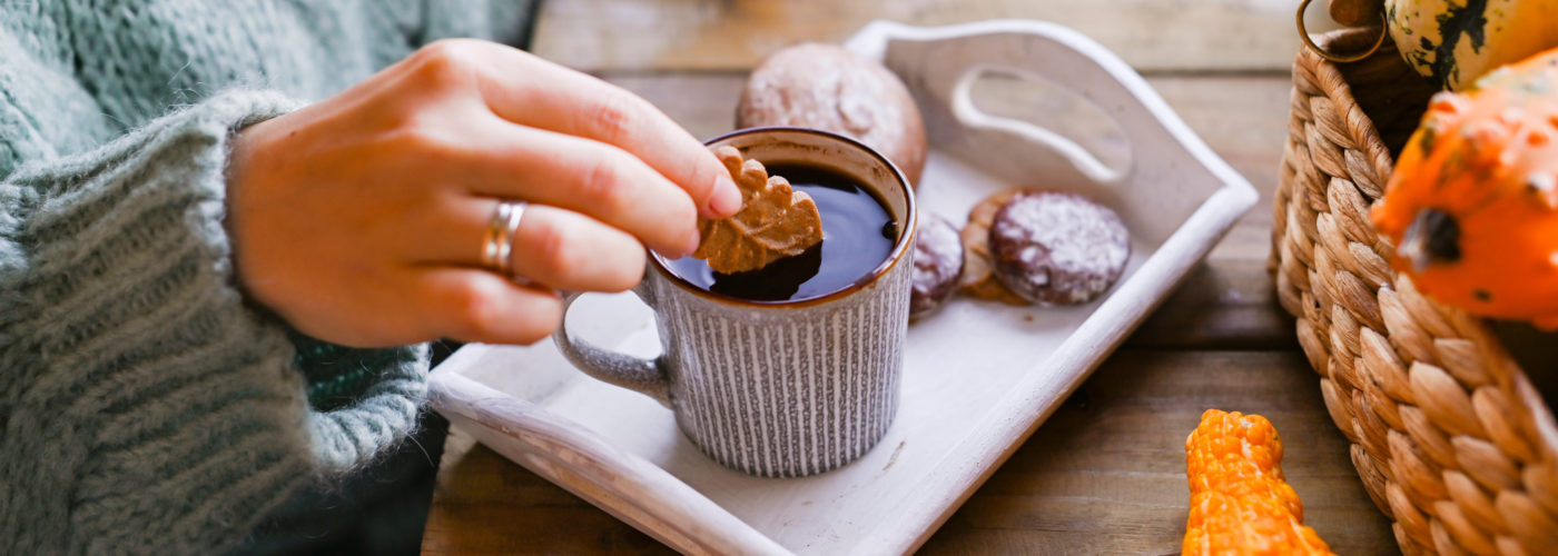 Close up of a woman dipping a cookie into a mug of coffee on a table set up with fall decor and desserts