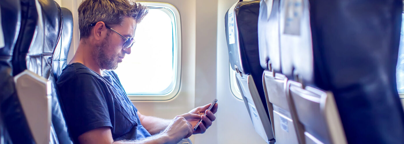 Man with dark hair is reading text message on mobile phone in airplane seat