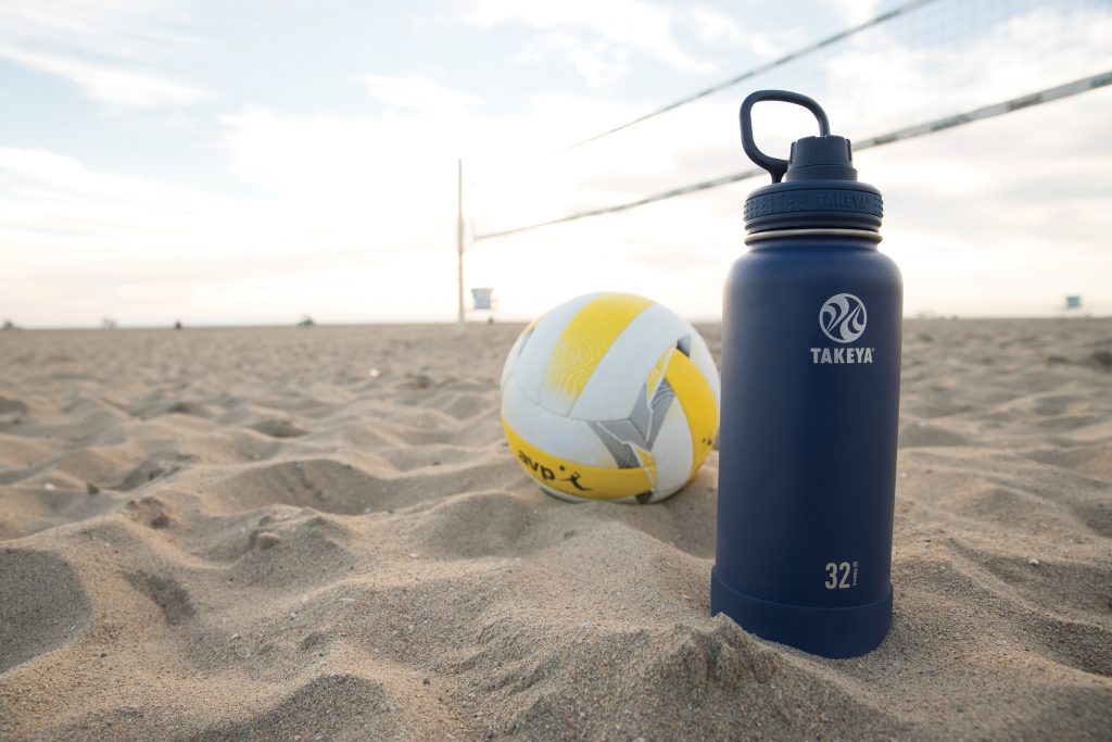 Takeya Actives Water Bottle in the sand on the beach by a volleyball net