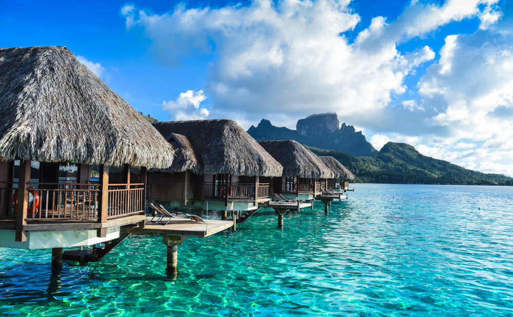 row of overwater bungalows in tahiti with mountain distance