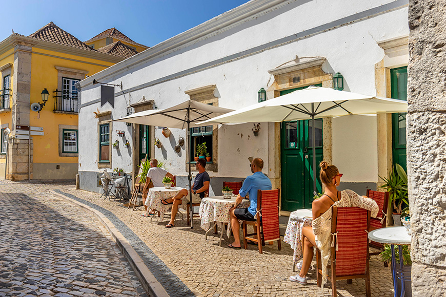 Die Leute sitzen auf der Außenterrasse eines kleinen Cafes im historischen Zentrum von Faro