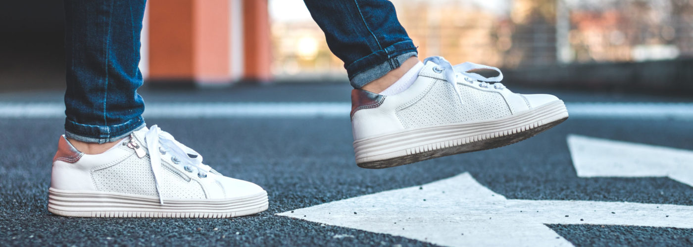 Close up of a person wearing white sneakers crossing the street