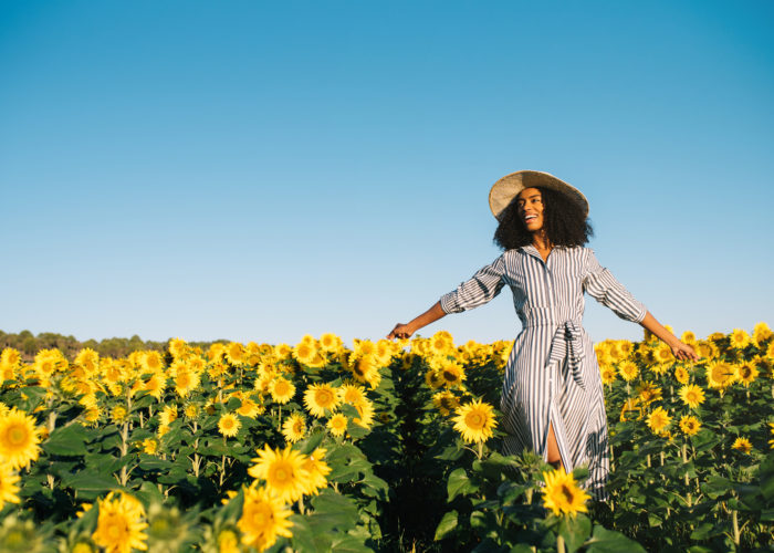 Woman in sundress and sunhat walking through a field of sunflowers on a clear day