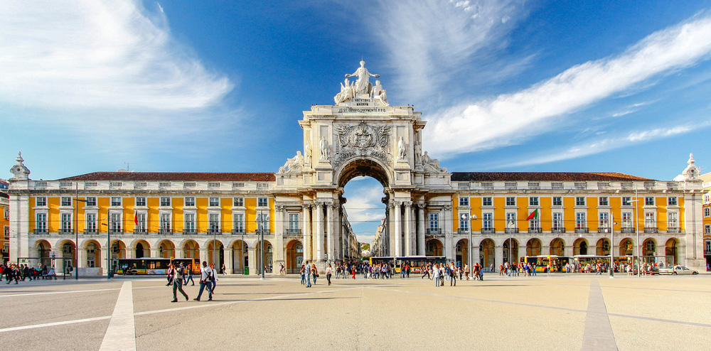 a long yellow building with columns and a large arch in the middle front of huge square