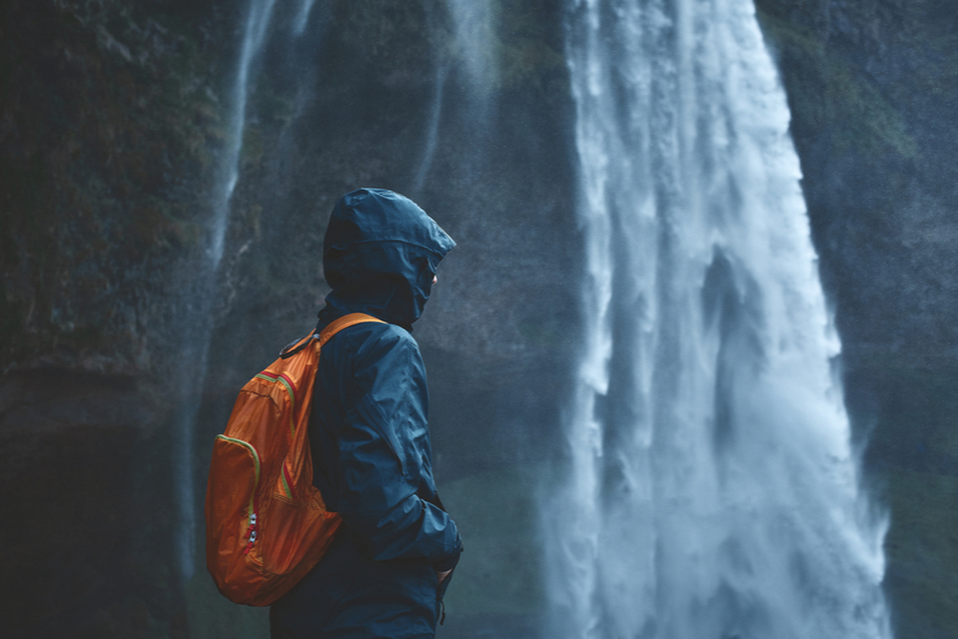 woman in waterproof clothes standing by waterfall.