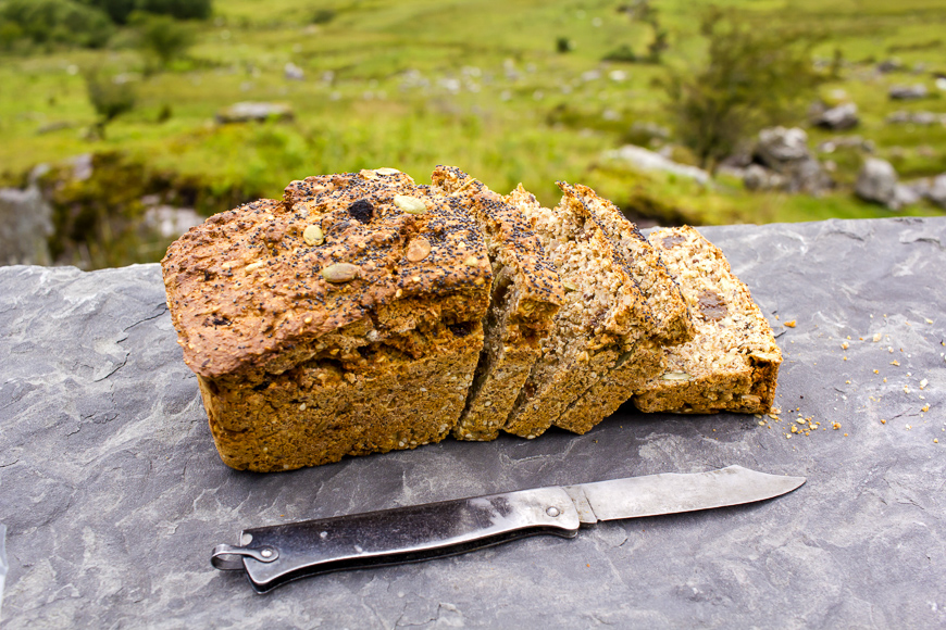 Sliced loaf of the fresh traditional Irish soda bread outside with knife aside and visible greenery on the background.