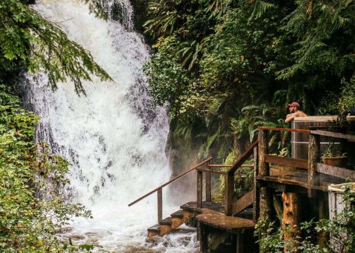 man sits in hot tub by waterfall in Nimmo Bay Wilderness Resort