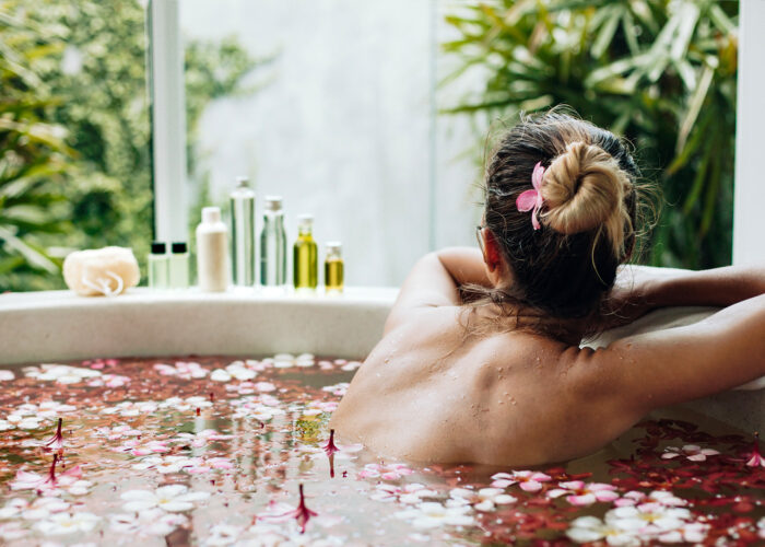 women in bath filled with rose petals and essential oils on the side
