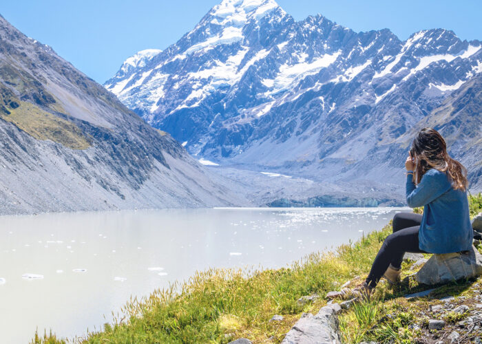 Woman Sits on the Edge of Hooker Glacier Lake with Aoraki Mt. Cook in the Background