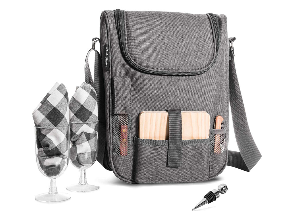 A picnic backpack carrying a cheeseboard and knives, with wine glasses and a bottle stopper next to it