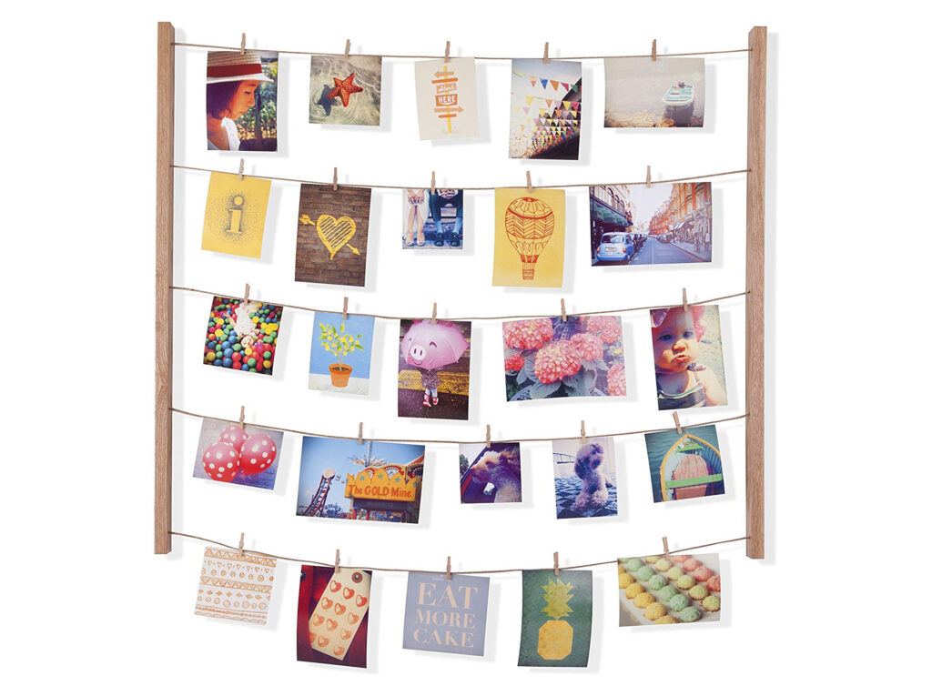 A photo display board made from two wooden sticks with string connecting them, small photos hanging from the string