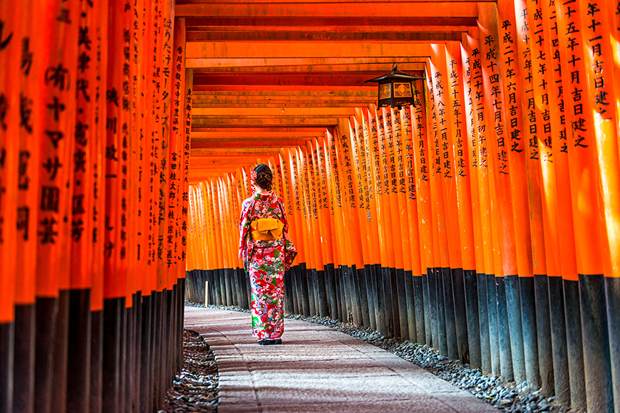 Women in kimono walking at Red Torii gates in Fushimi Inari shrine, one of famous landmarks in Kyoto, Japan