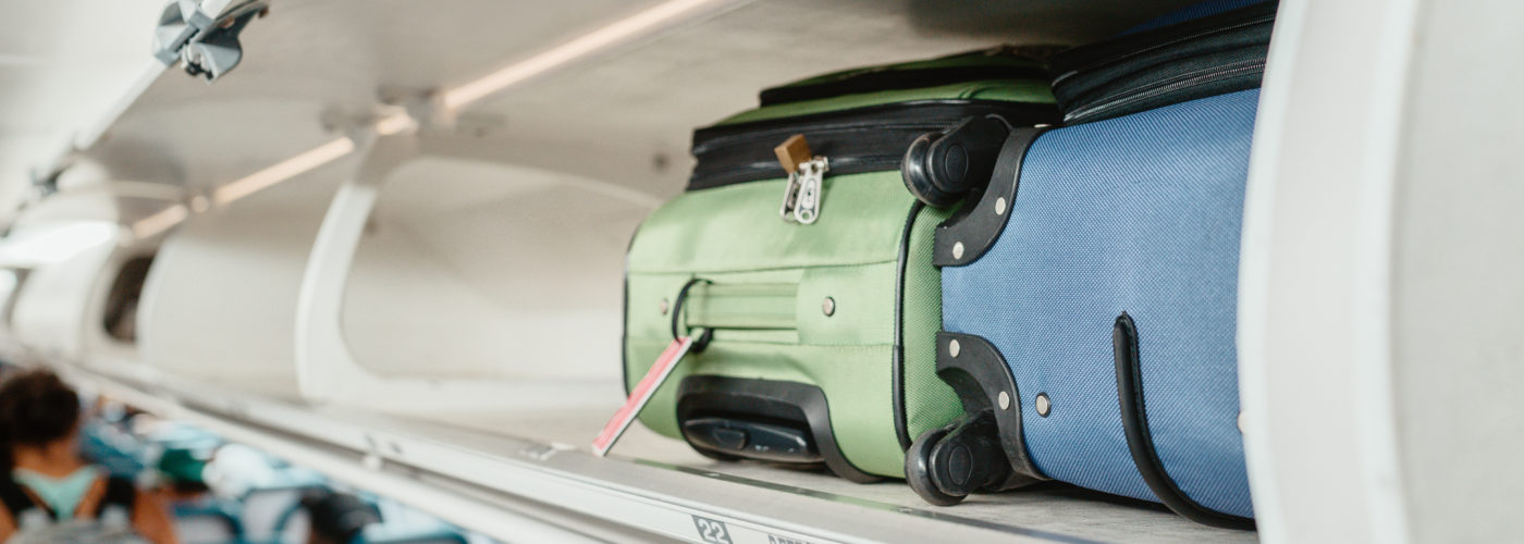 Two suitcases, one green and one blue, in the overhead bin of an airplane