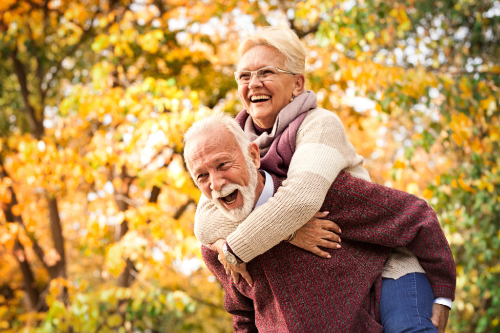 An elderly man giving an elderly woman a piggy back ride outdoors,