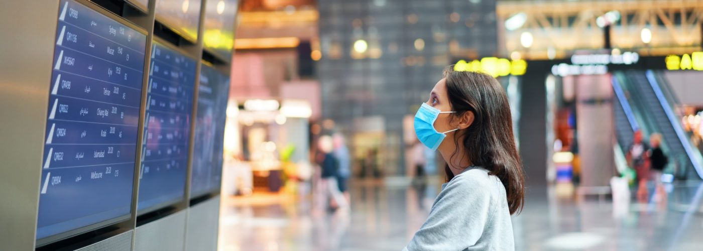 Woman in face mask looking at information board checking her flight in international airport