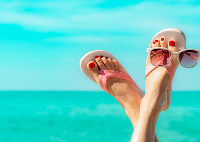 Feet wearing flip flops and holding sunglasses between the toes