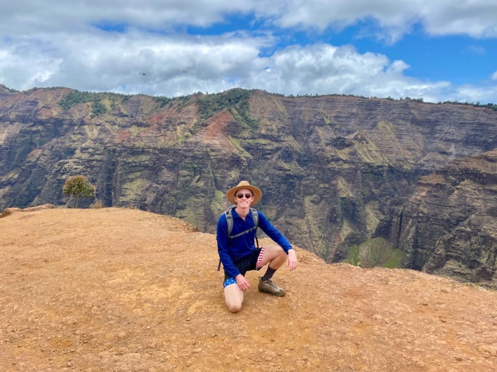 Man kneeling on a cliff in front of a large rock face