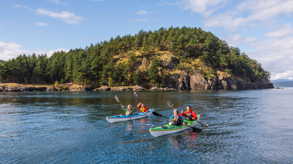 Two kayaks full of people on a lake in front of a mountain