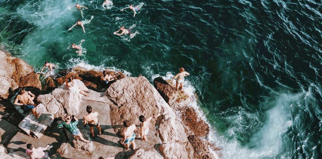 Group of young people jumping off cliff into water below