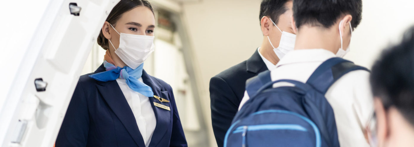 Masked flight attendant greeting passengers