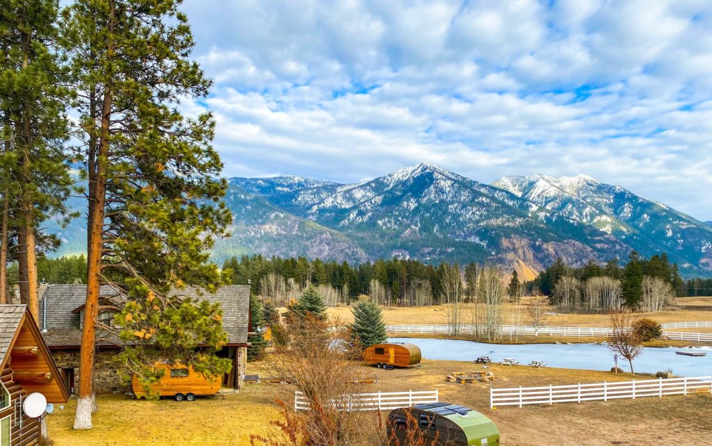 Two cabins and two small wooden trailers surrounded by trees on a backdrop of tall mountains at ROAM Beyond