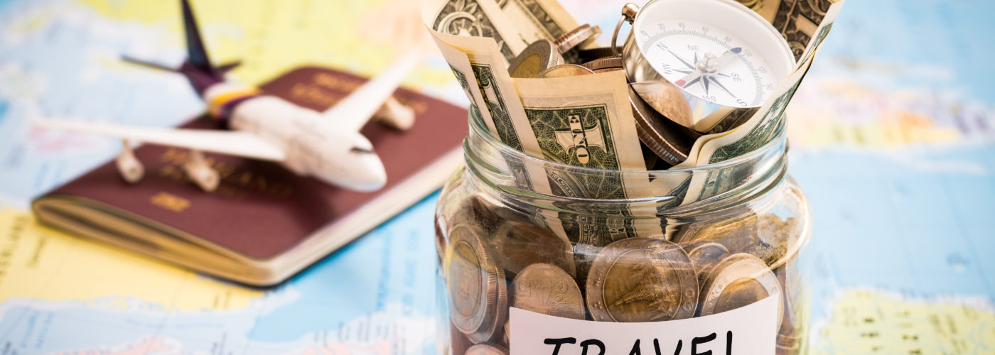 A jar of money labeled "Travel", a passport, and an airplane figurine on a colorful world map