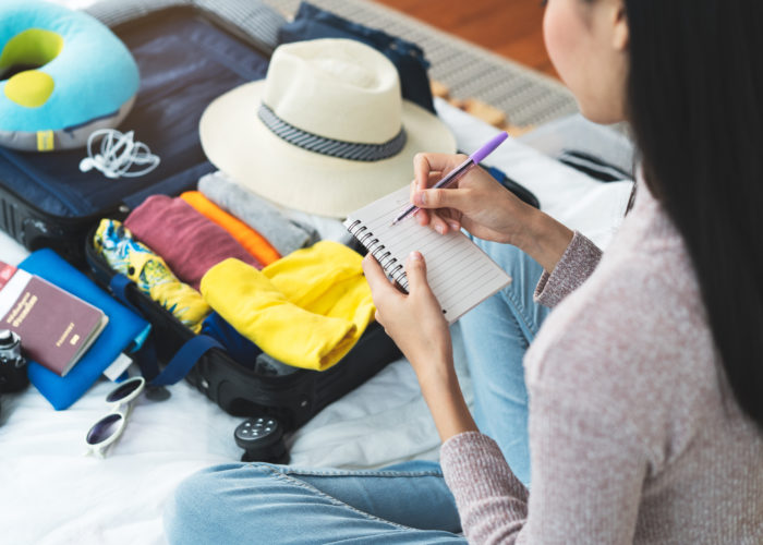 Woman makes a packing list on a small notepad while packing a suitcase