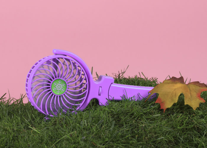 Handheld electric fan on a bed of grass with a pink backdrop