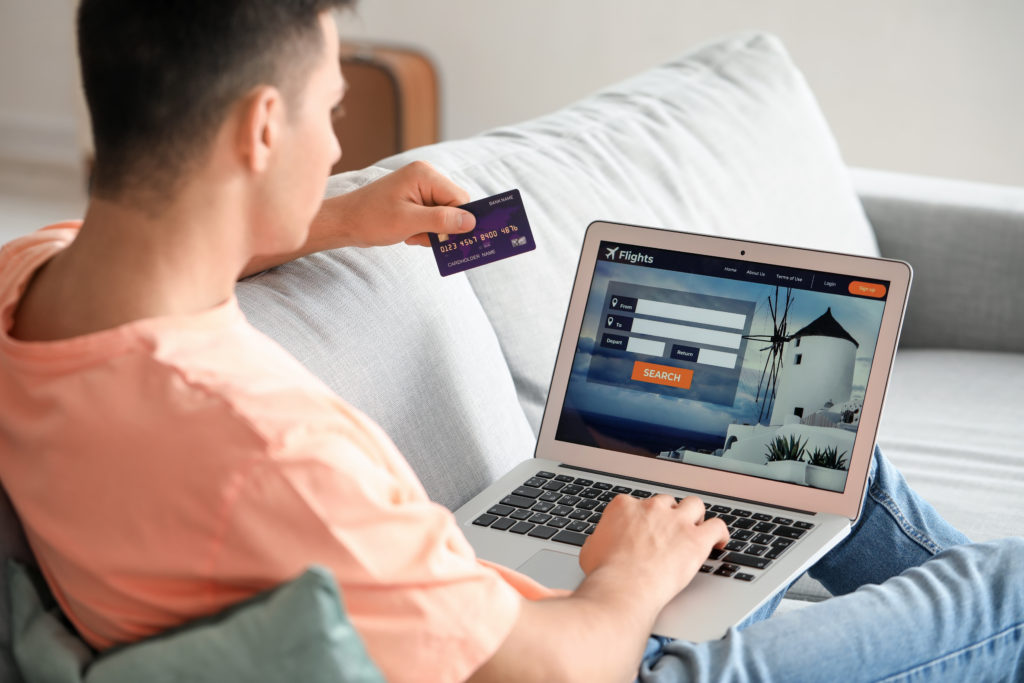 Man booking flights on the couch with his laptop and a credit card