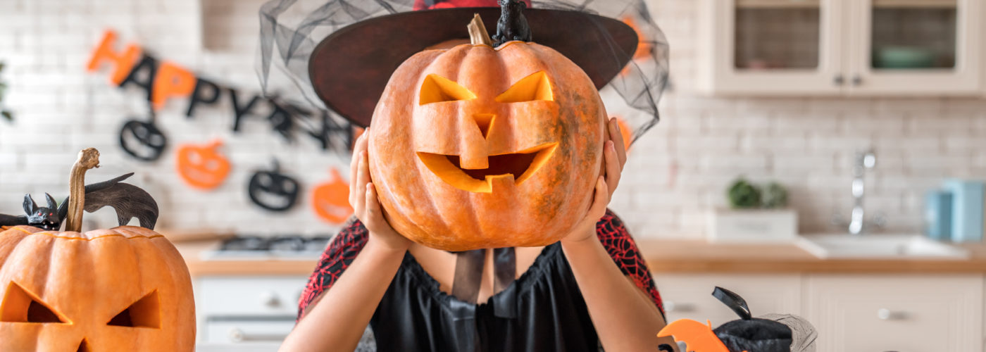Woman dressed as a witch holding a jack-o-lantern in front of her face