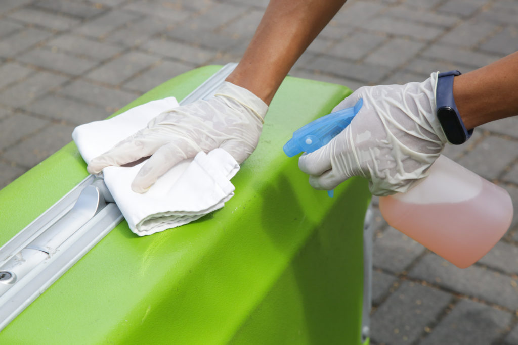 Person wearing gloves cleaning a green suitcase with a towel and spray cleaner