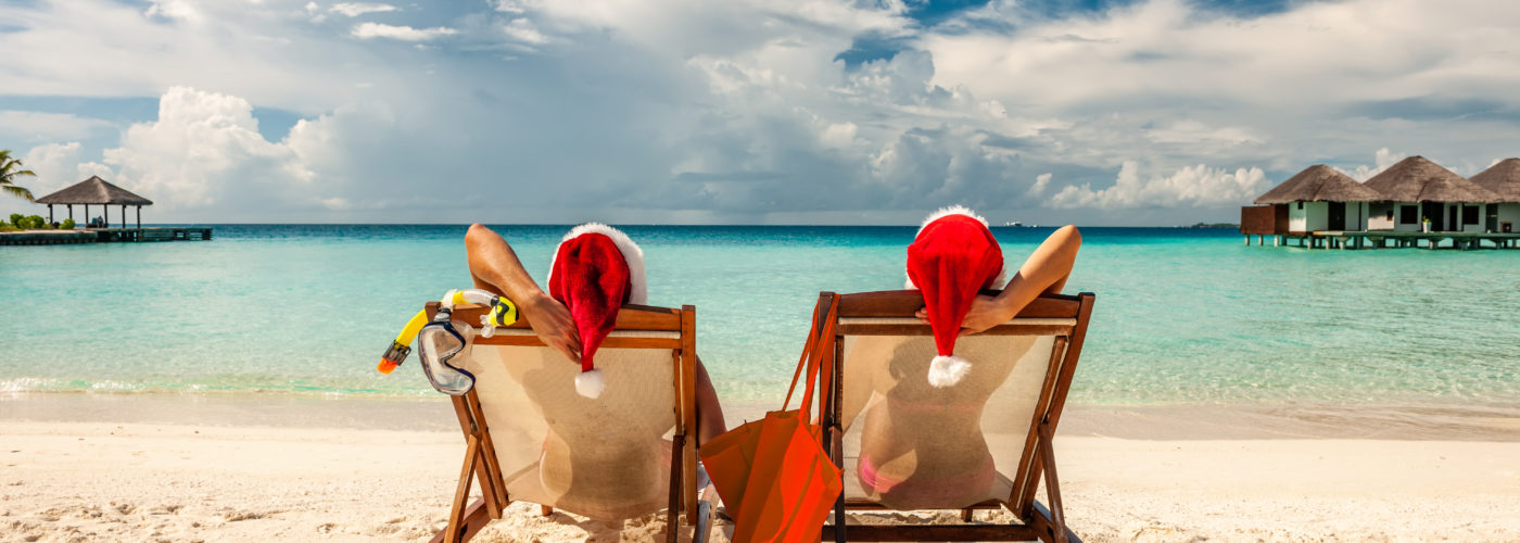 Couple sitting on lounge chairs on the beach in Santa hats