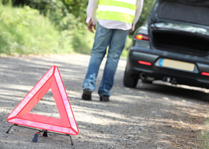 Man setting out hazard triangle from car emergency kit at breakdown