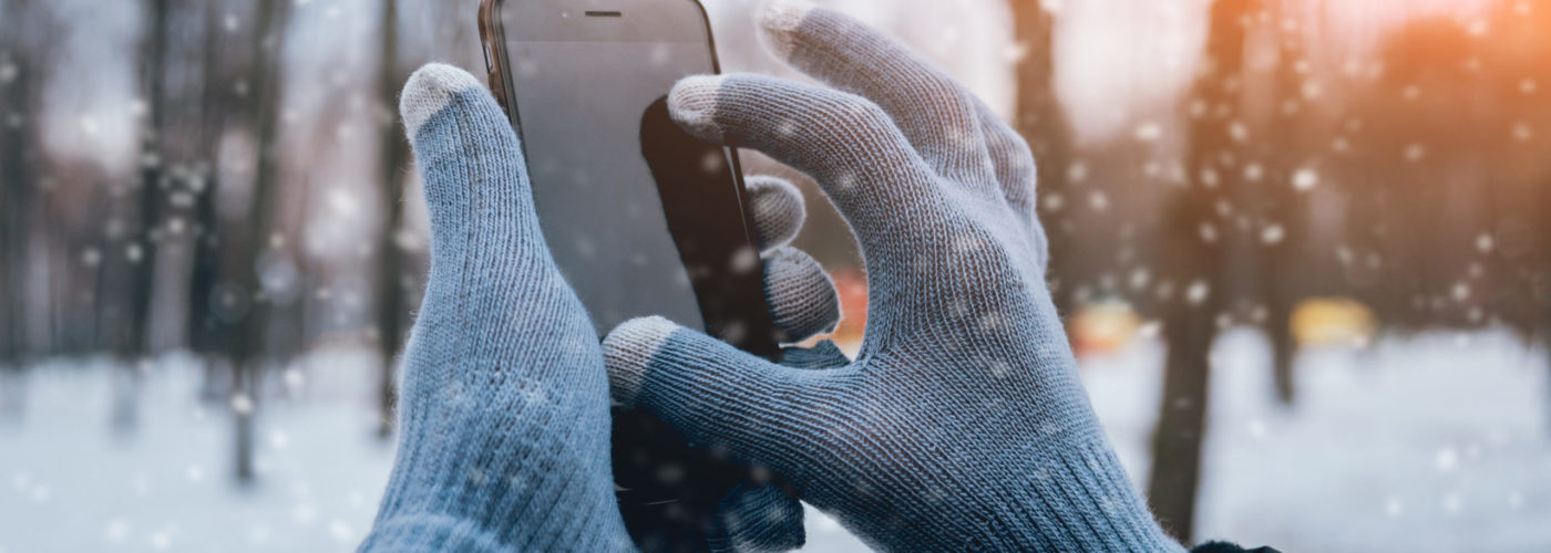 Close-up of hands wearing gloves while using a touchscreen smartphone