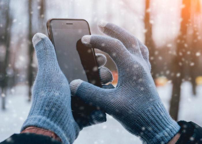 Close-up of hands wearing gloves while using a touchscreen smartphone