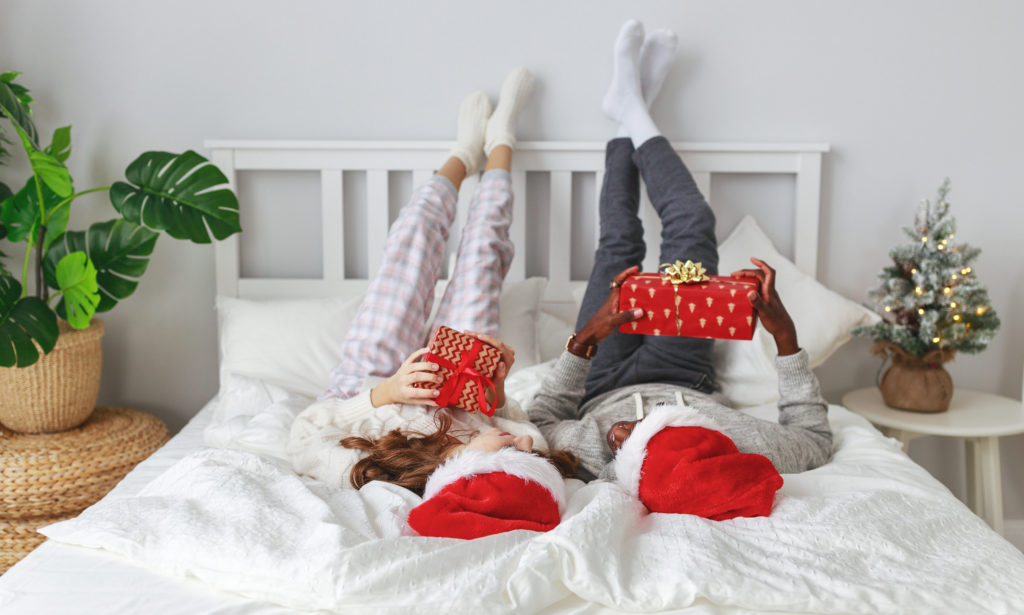 Couple on bed in holiday pajamas holding gifts