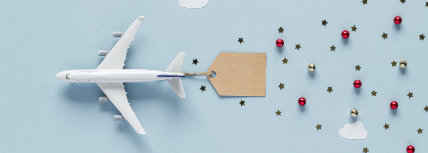 A toy plane on a blue backdrop attached to a tag with small Christmas ornaments trailing behind it