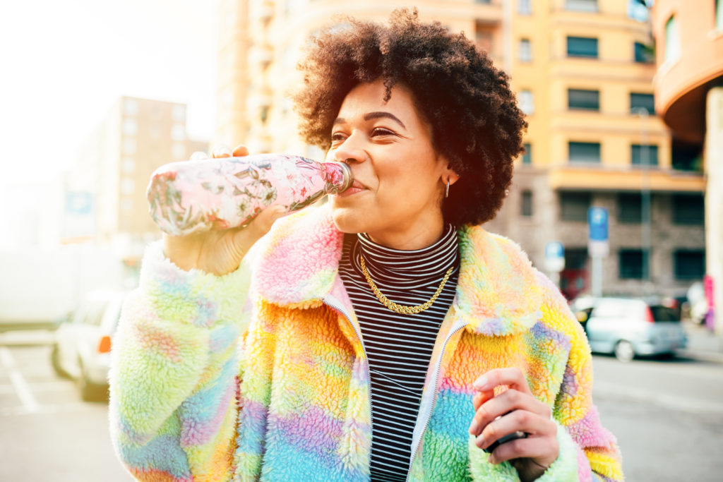 Woman in colorful coat drinking from a reusable water bottle