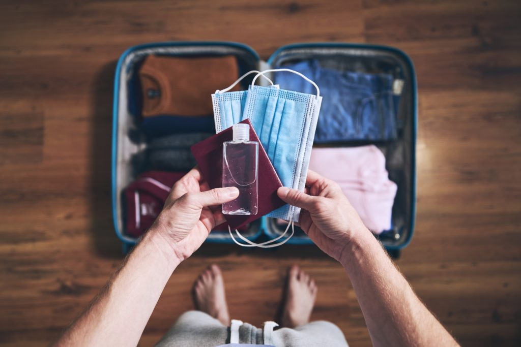 Aerial view of person packing a face mask, passport, and hand sanitizer for a trip