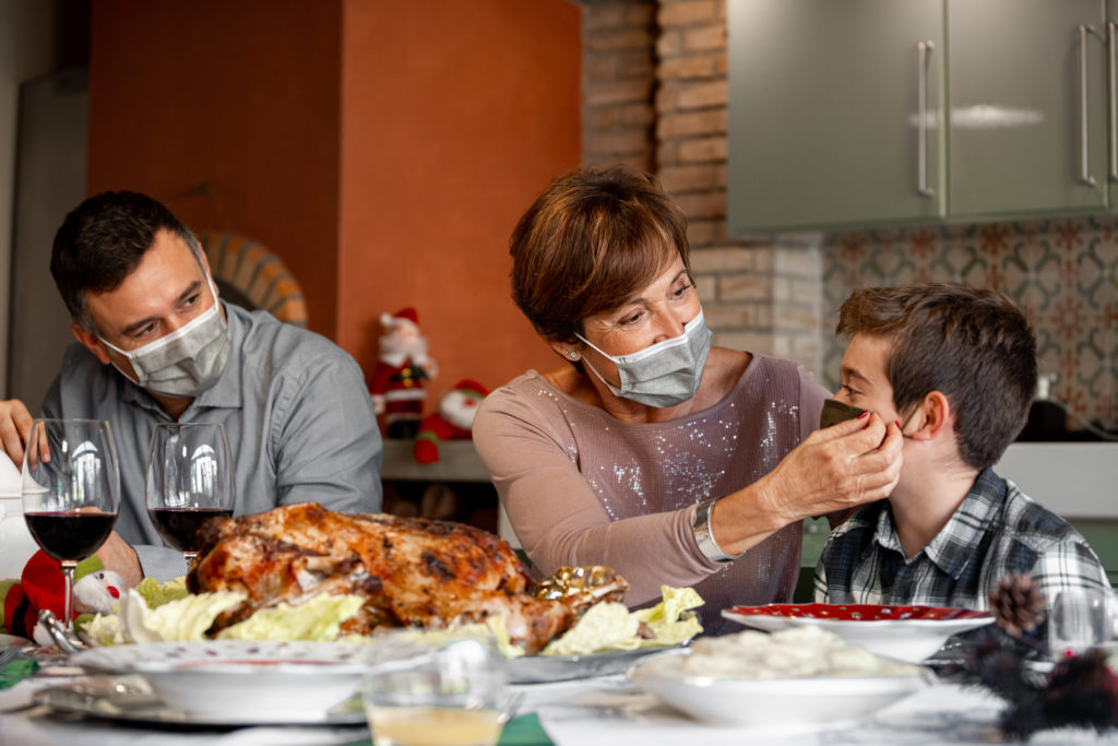 Family member helping child put on a face mask at a family holiday meal