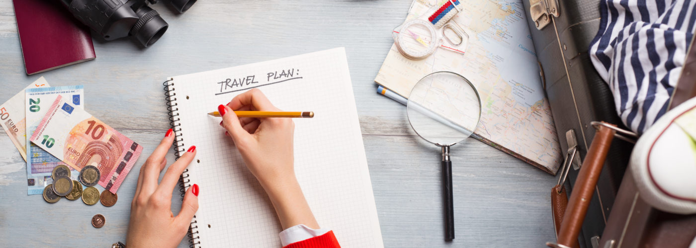 Overhead view of someone planning their trip in a notebook surrounded by travel items