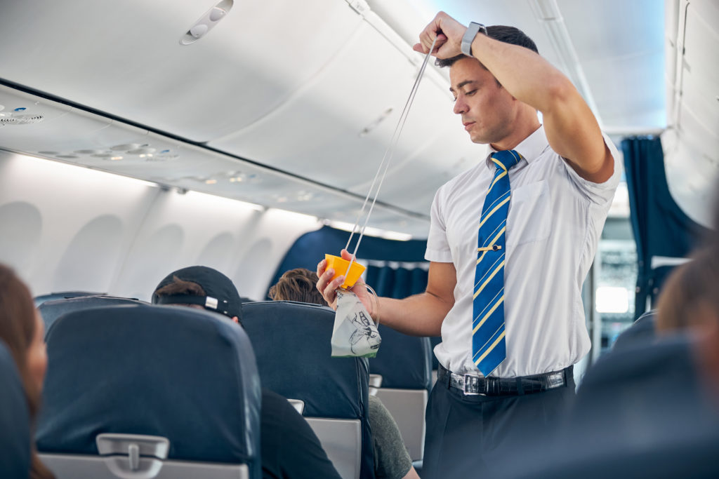 Flight attendant demonstrating use of oxygen mask in airplane cabin