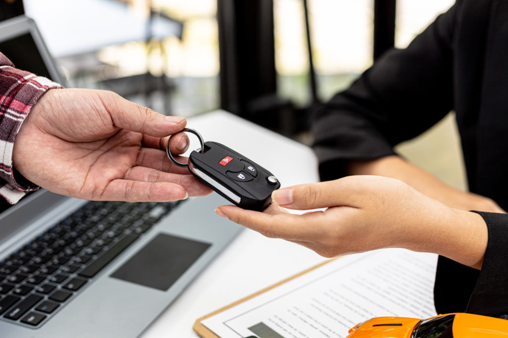 Close up of hands exchanging a key for a rental car over a desk