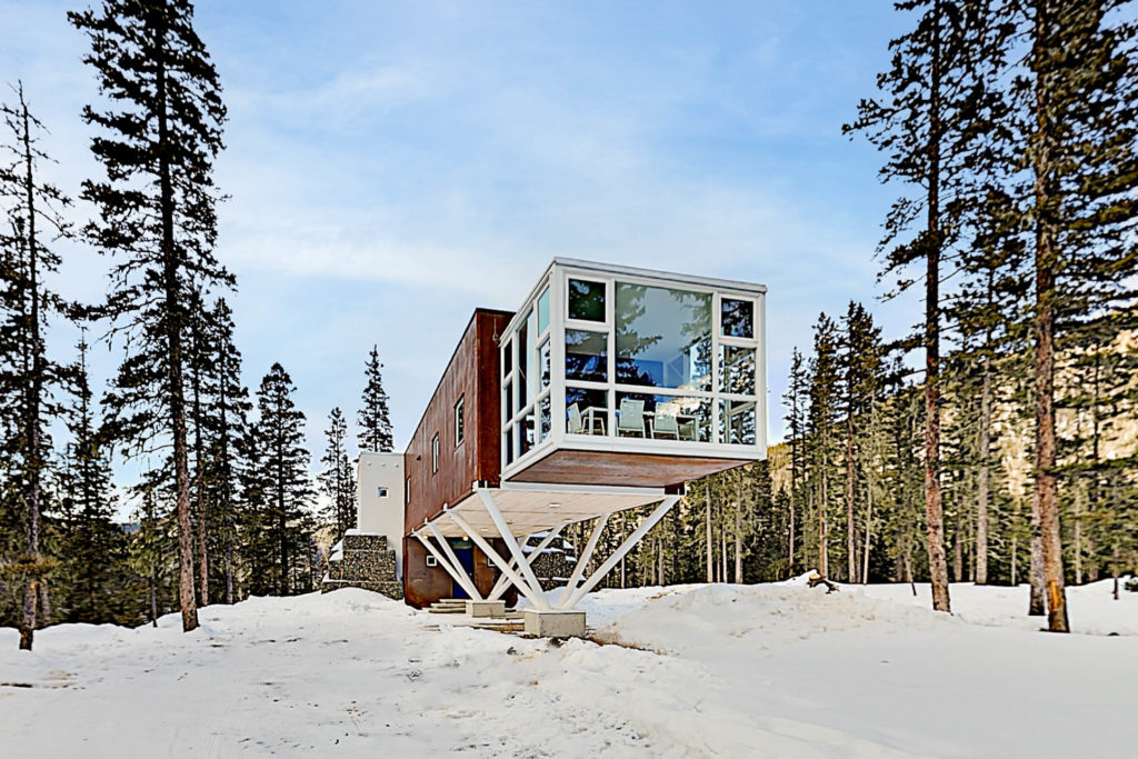Cabin standing on white wooden support beams in the middle of a snowy forest