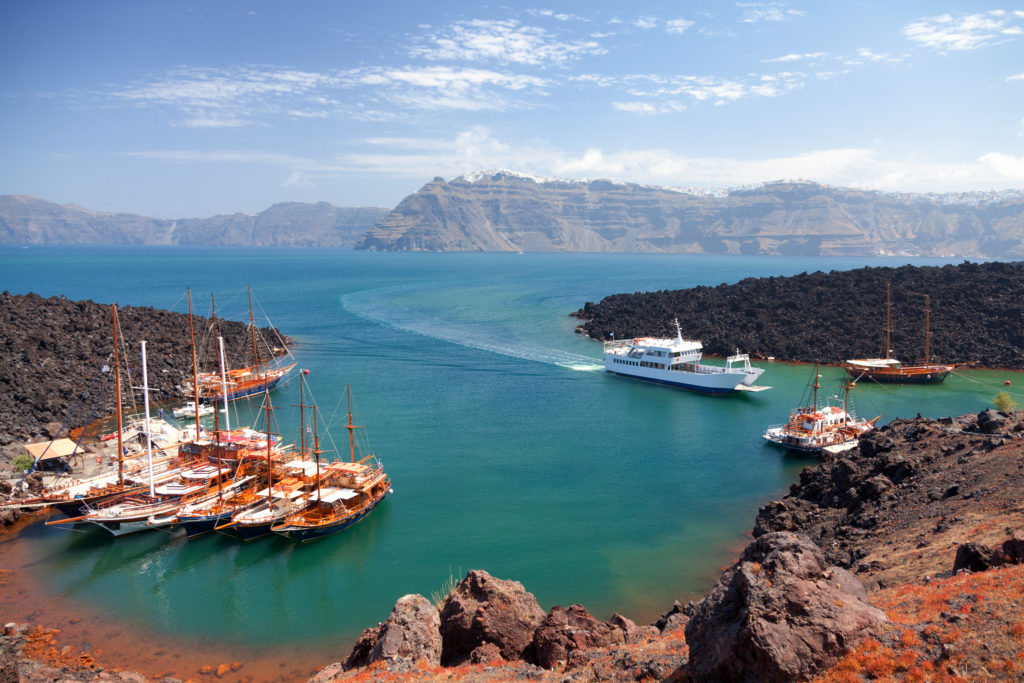 Small inlet filled with ships on Nea Kameni volcanic island in Santorini, Greece