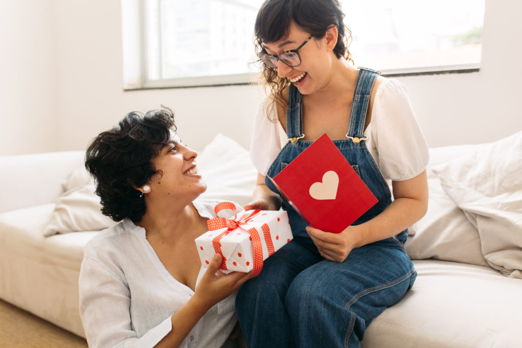 Couple exchanging Valentine's day gifts, one sitting on the couch and one sitting on the floor