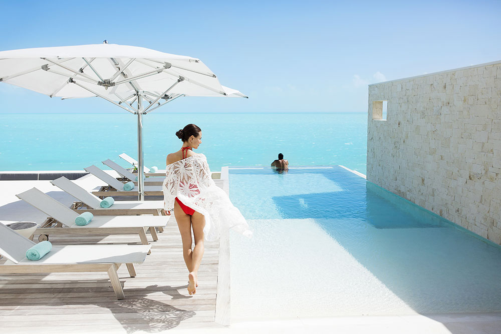 Woman walking on pool deck toward man in infinity pool at Wymara Villas, Turks and Caicos