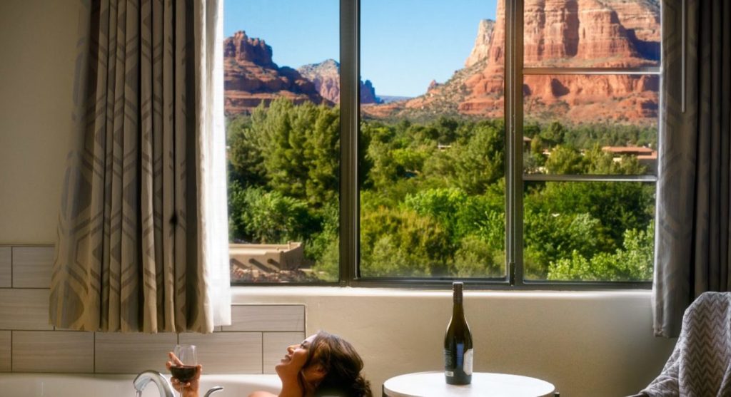 Woman relaxing in bathtub next to a window with views of large rock formation at the Hilton Sedona Resort at Bell Rock, Arizona