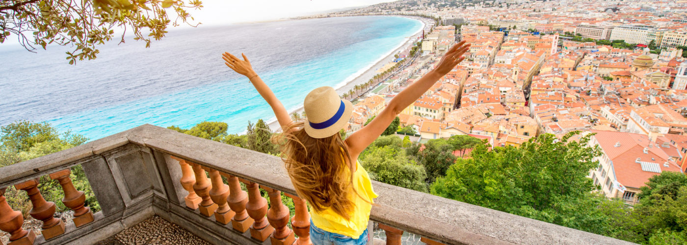 Woman with her arms raised on balcony overlooking Nice, France on a sunny day