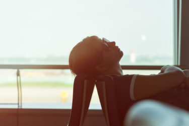 Woman backlit by airport window resting her head on a chair in an airport terminal